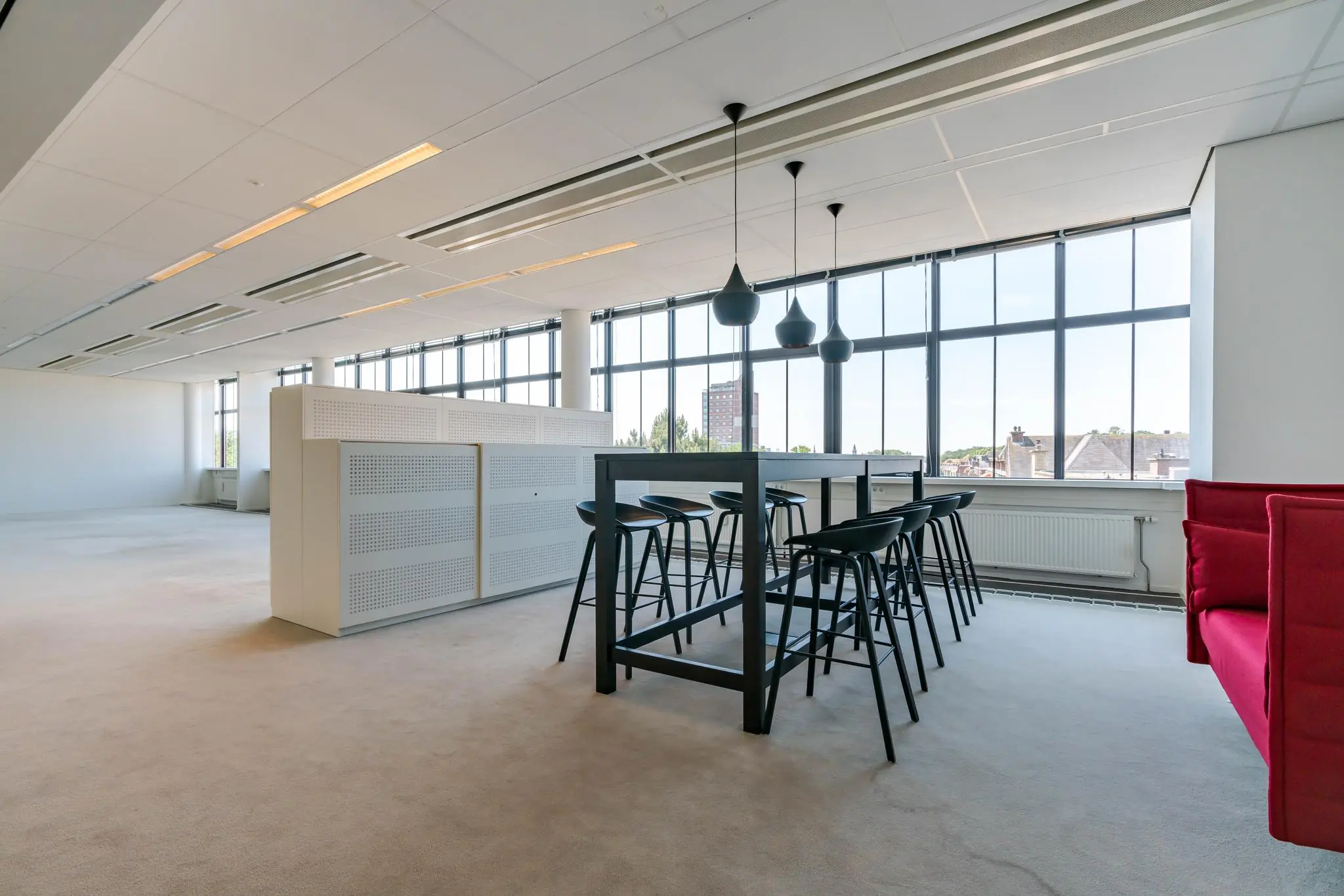 Moderne kantoorruimte aan de Van Alkemadelaan met hoge ramen, een zwarte vergadertafel en designverlichting.